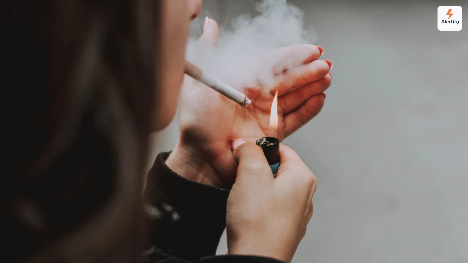 Persoană care aprinde o țigară în interior, cu fum ridicându-se în jurul mâinilor
