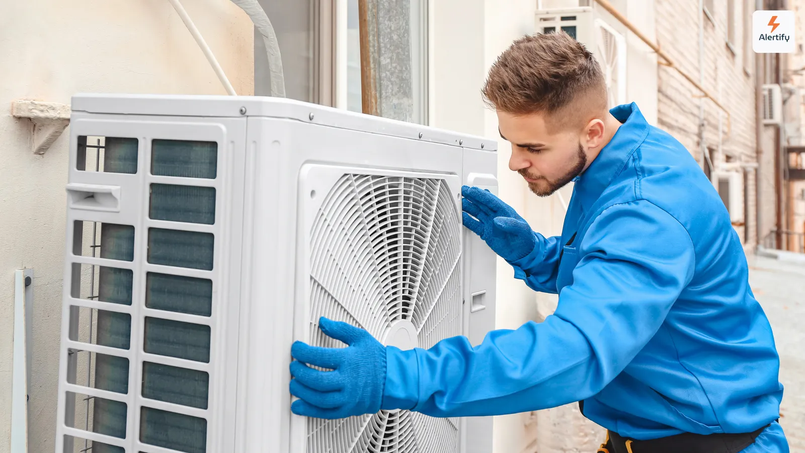 Tehnician HVAC în salopetă albastră și cu mănuși, efectuând service la o unitate exterioară de aer condiționat