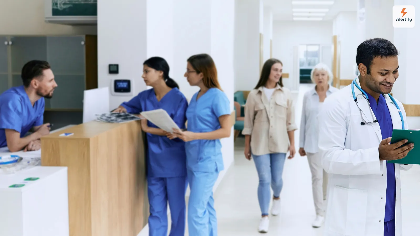 Medici și vizitatori trecând pe lângă recepția din holul luminos al unui spital
